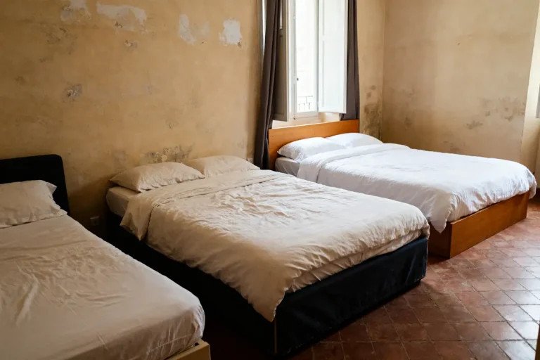 Trois lits de tailles différentes alignés dans une chambre avec mur beige défraîchi