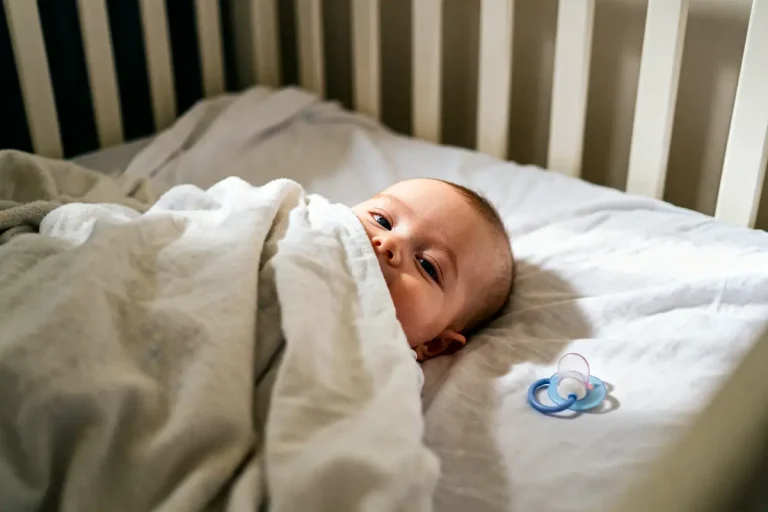 Bébé endormi dans un lit avec tour de lit dangereux et tétine bleue sur le matelas