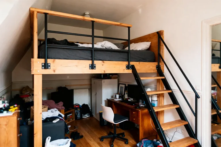Mezzanine en bois avec lit, échelle, bureau en dessous, chambre encombrée, chaire pivotante, parquet.