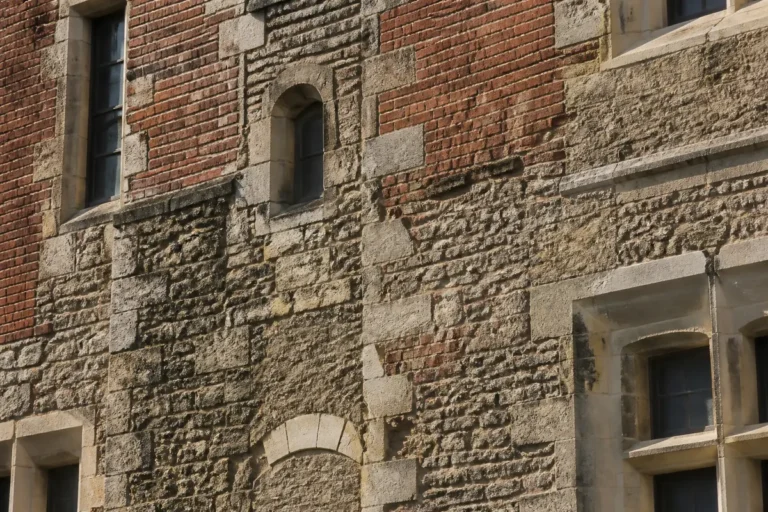 Façade en briques et pierres, fenêtre en arc et fenêtre rectangulaire, style architectural historique.